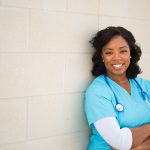 A smiling nurse leaning against a wall.