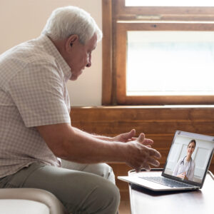 An older patient talking to their GP using a laptop.