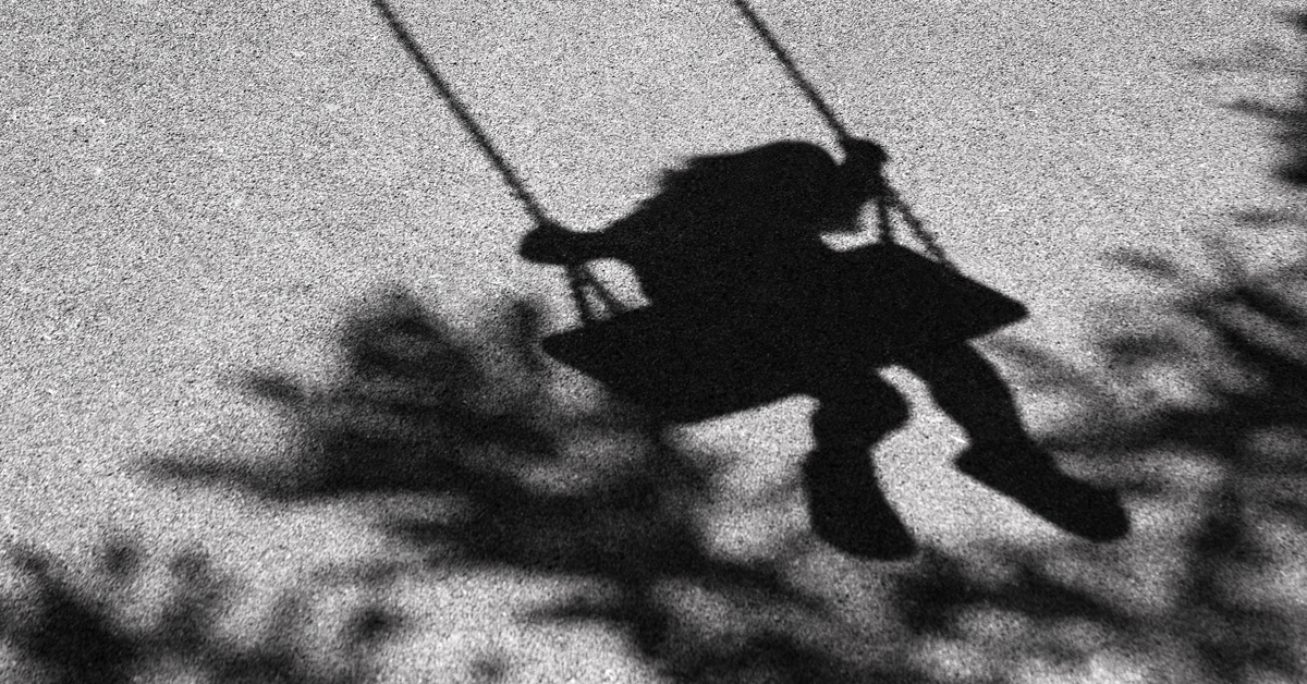 Shadow of a young child on a playground swing.