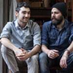 2 men sitting on a set of stairs in conversation.