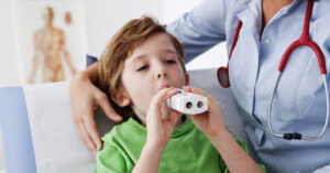 A young child using an asthma inhaler under supervision from a practice nurse.