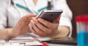 An unidentified female doctor checks her phone at her desk