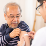 A young male GP places a band-aid on the upper arm of an elderly patient after administering a vaccine