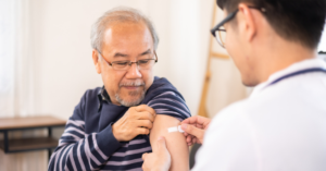 A young male GP places a band-aid on the upper arm of an elderly patient after administering a vaccine