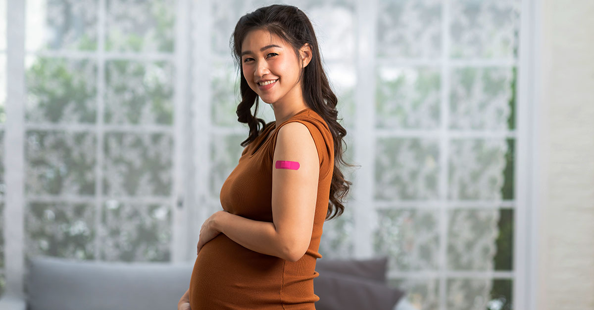 A pregnant woman smiles after receiving a vaccination, with a band aid on her upper left arm