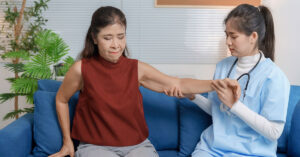 A nurse assists a middle-aged woman with arthritis lift up her arm