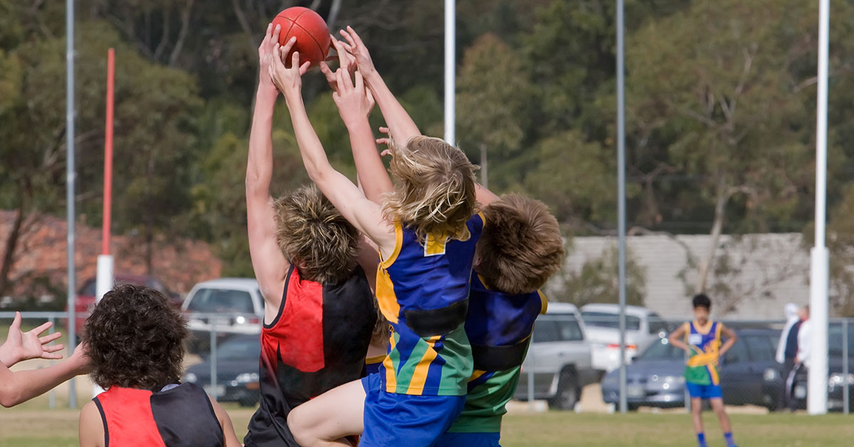 Junior Australian rules footballers jump to mark the ball